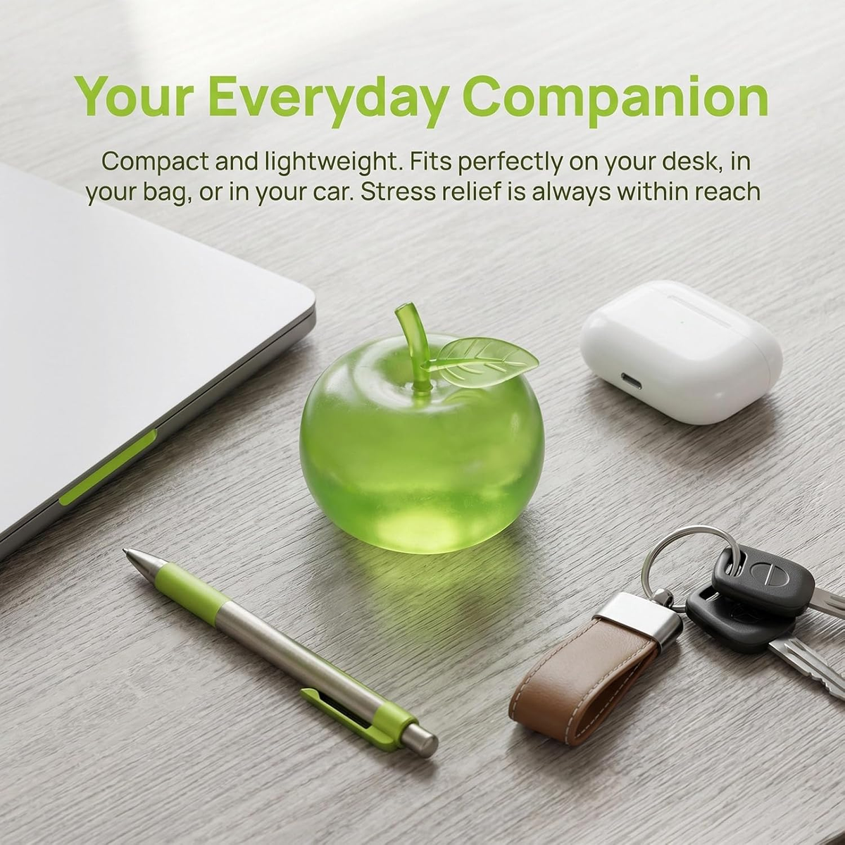 Green apple squishy on a desk beside a laptop, pen, earbuds and keys