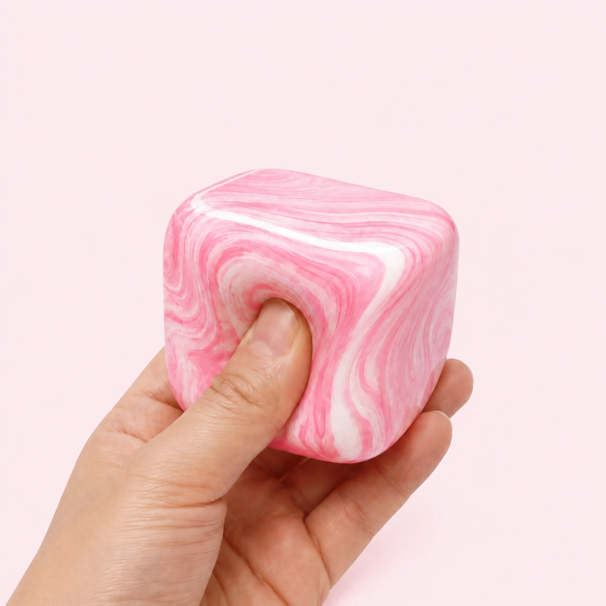 Hand squeezing the pink and white Fluid Swirl Cube on a pale pink background